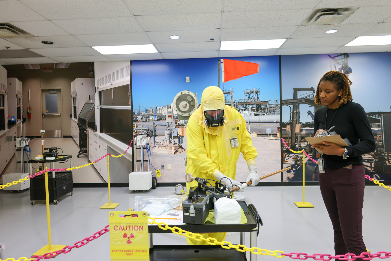 A man in a yellow hazmat suit working with a woman safety instructor in a lab