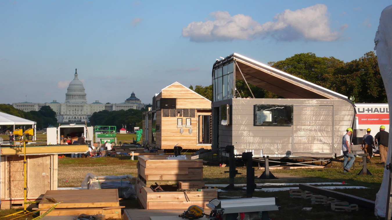 The site of the Build Challenge event on the National Mall in Washington, D.C., with a few competition houses in the foreground and the Capitol building in the background.
