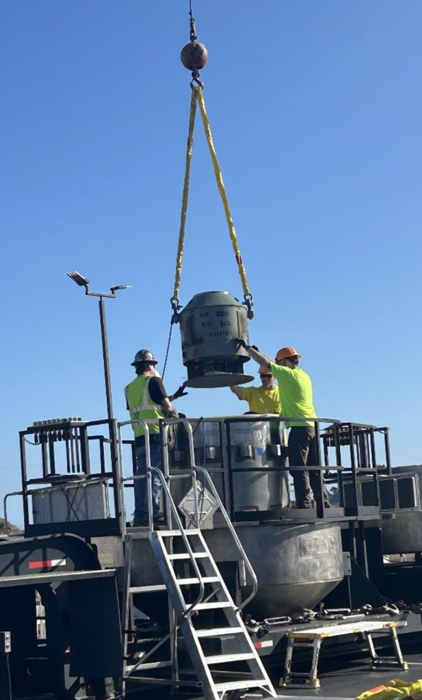 Two men in high-visibility clothing help lower a cesium irradiator into a cask for transport out of South Carolina.