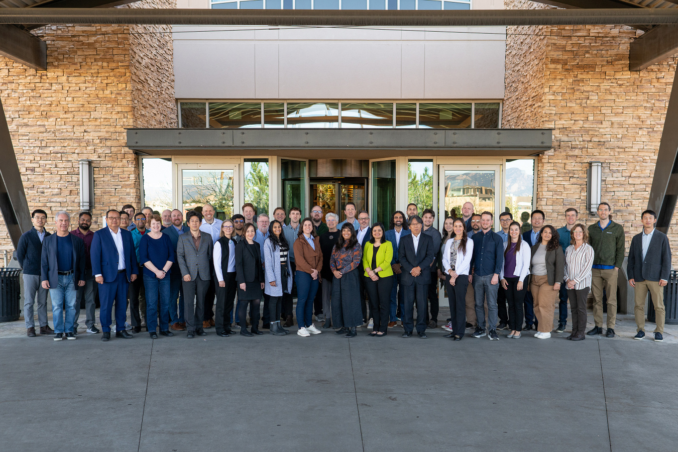 A group of approximately 45 people stand together in front of a hotel lobby. 