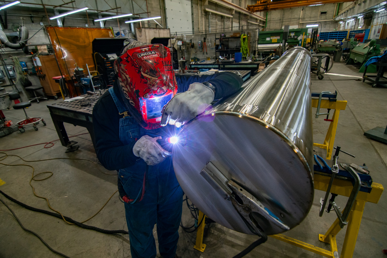 An employee in protective gear welding a metal rod in a laboratory