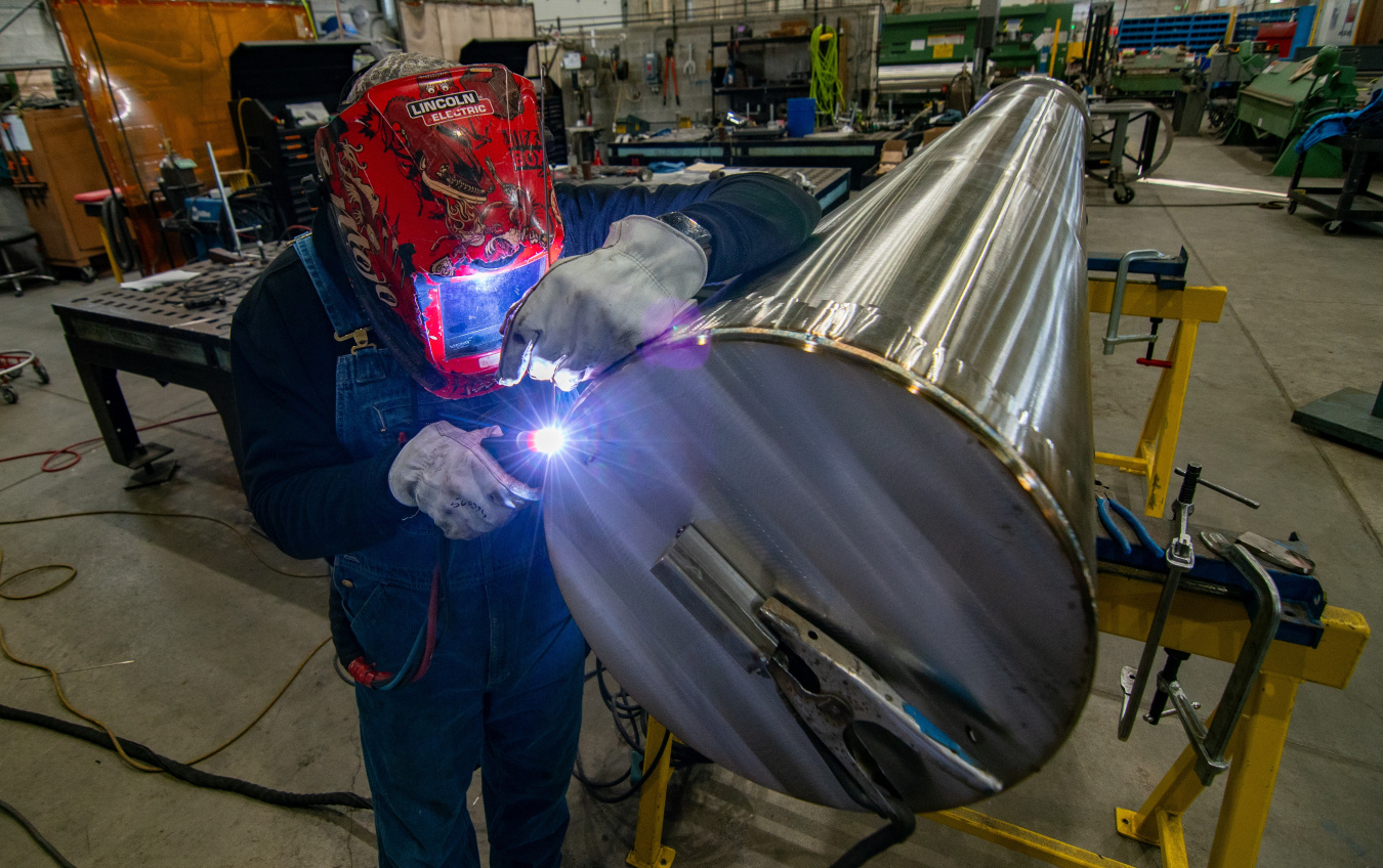 A person welding a large metal cylinder. 