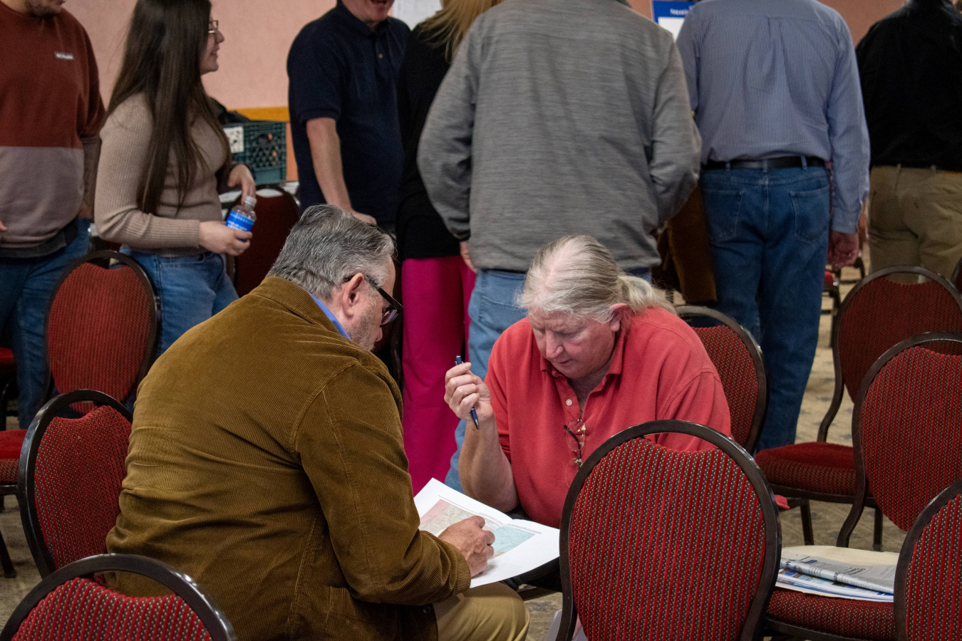 Two community members sitting in red chairs at a forum event