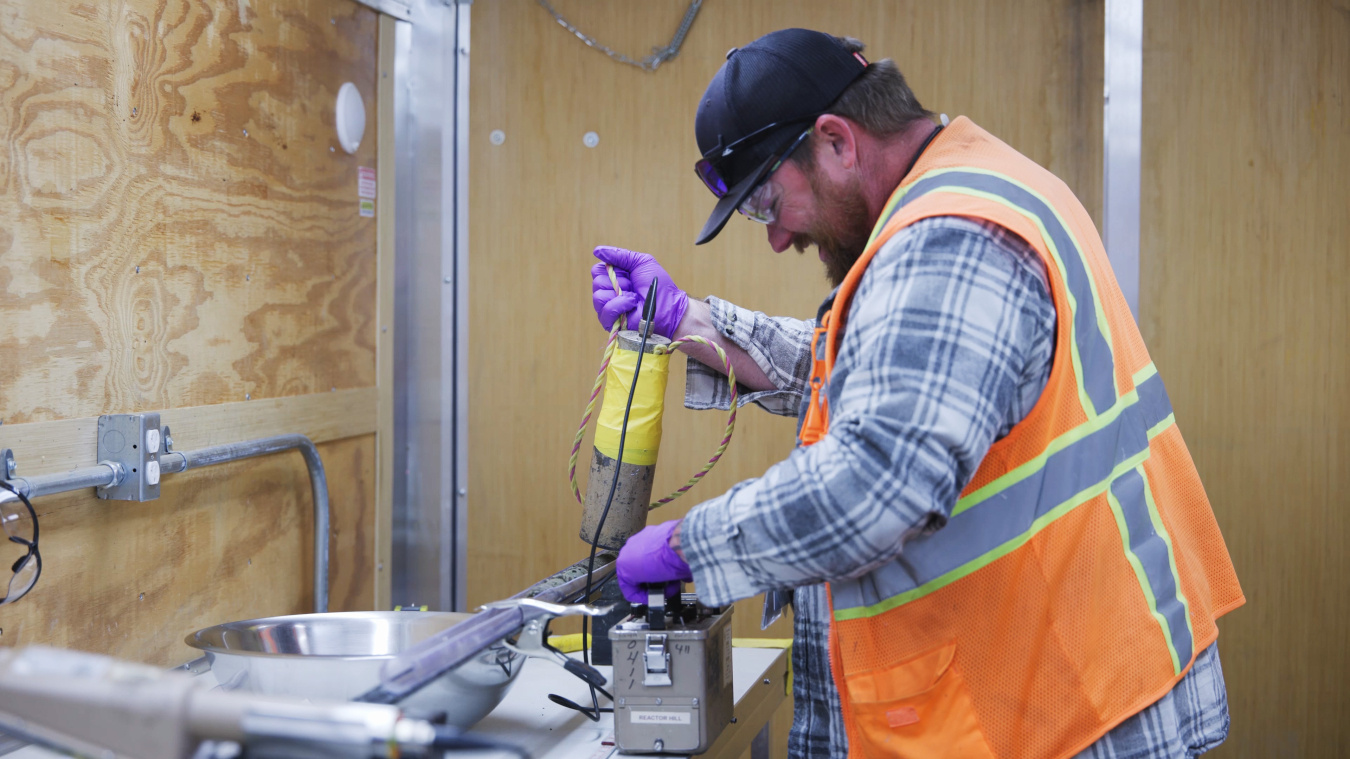 An employee in safety gear using tools to analyze samples at the Oak Ridge site