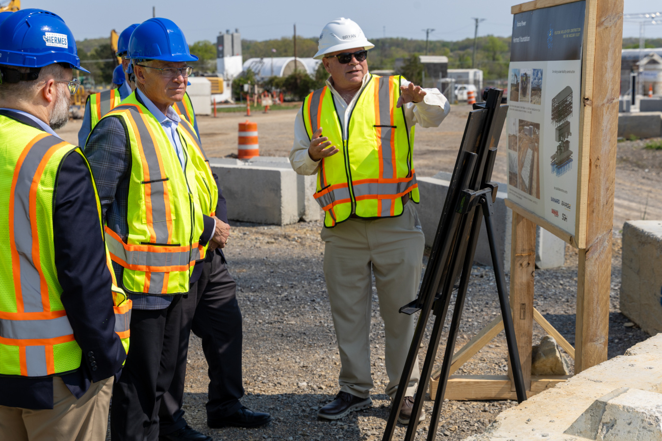 Men in safety vests and hard hats tour the outside of the Oak Ridge site
