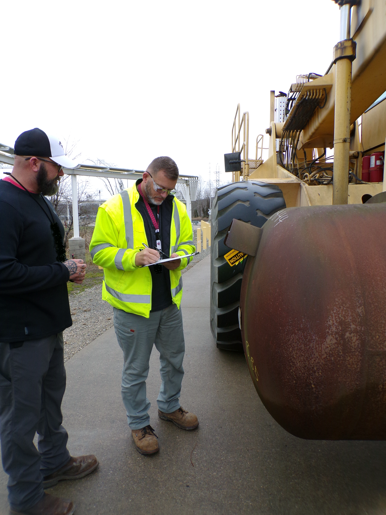 Two employees at the Portsmouth Site beside a large construction vehicle