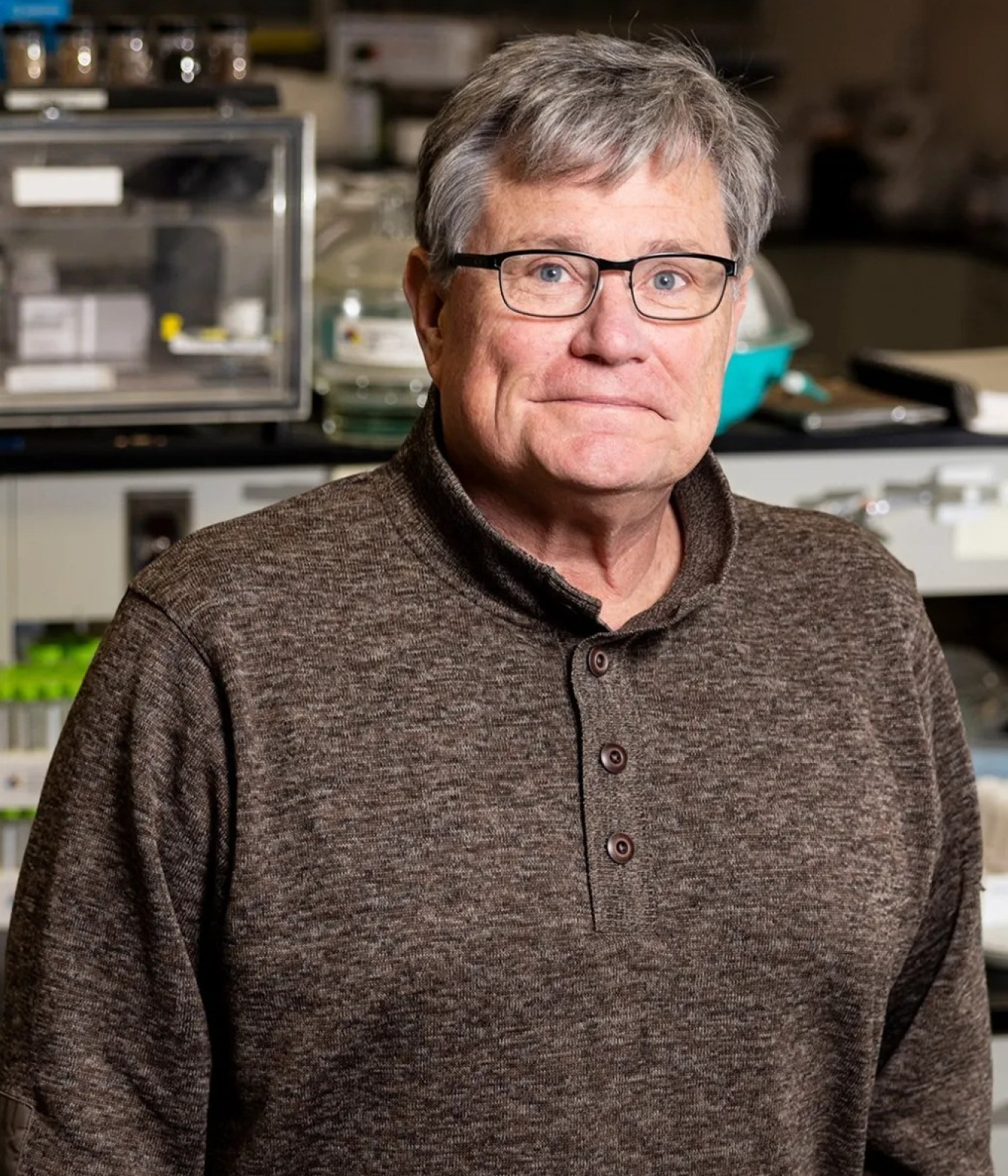 A headshot of an older gentleman wearing glasses inside a laboratory