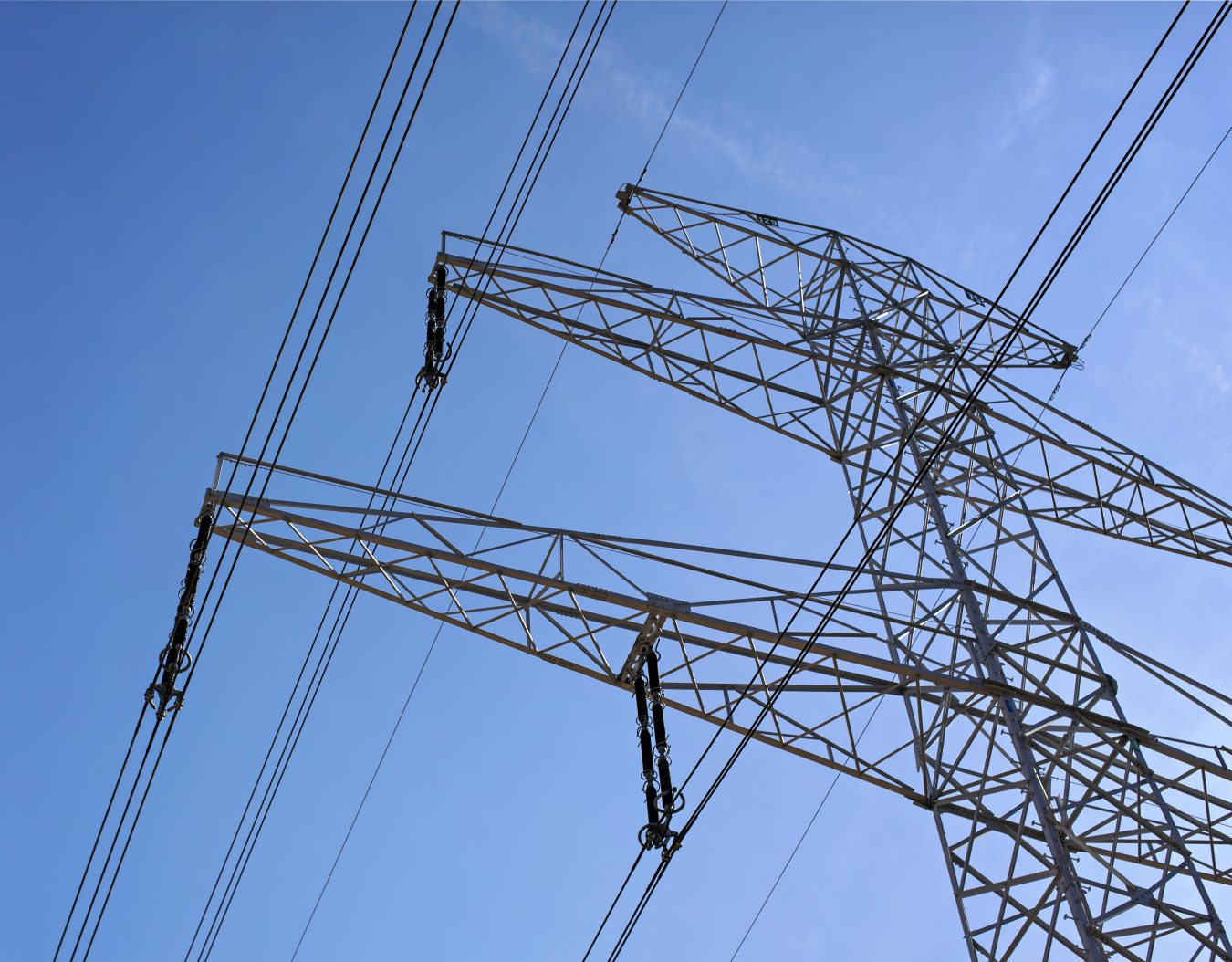 Looking up at a transmission tower and powerlines during daylight.