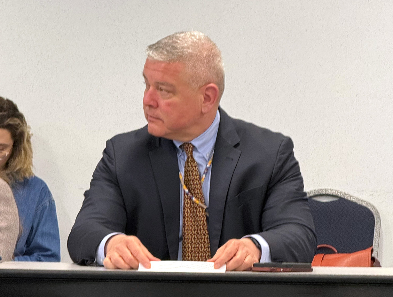 A person wearing a suit and tie at a desk.