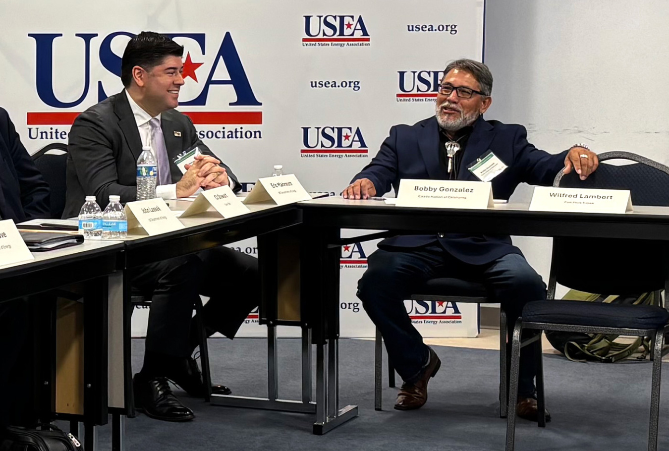 Two people wearing suits and ties sitting near each other on adjacent desks.