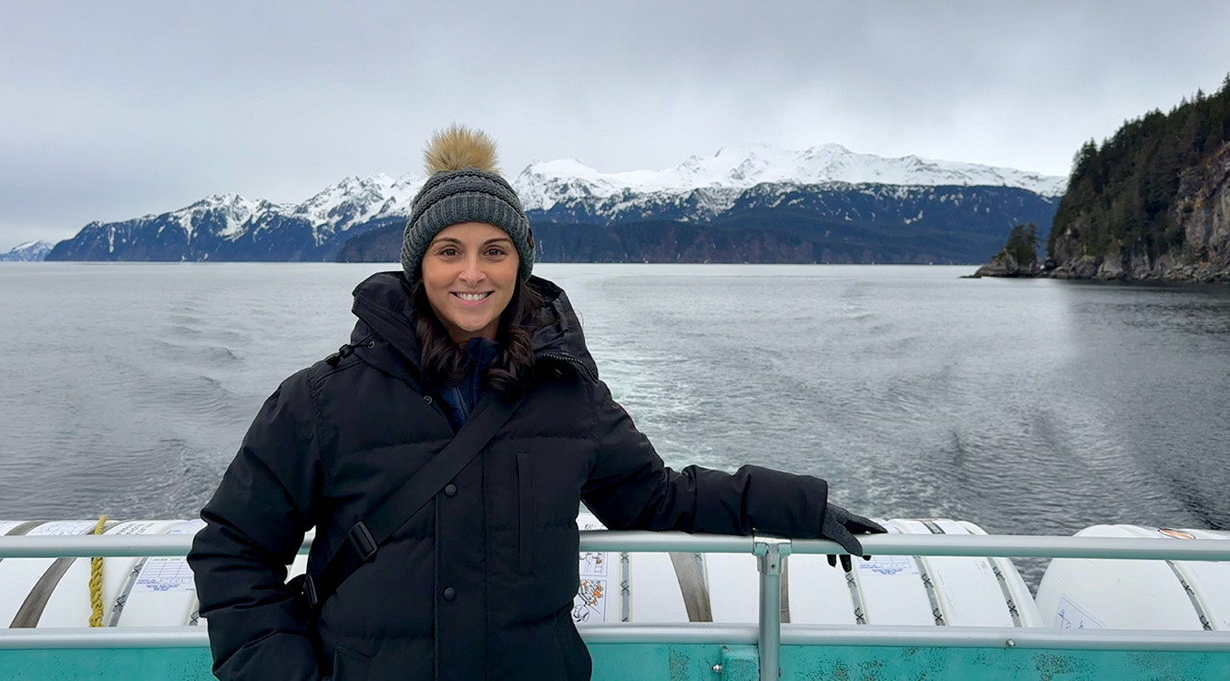 A person smiling on a boat with water and mountains behind them.