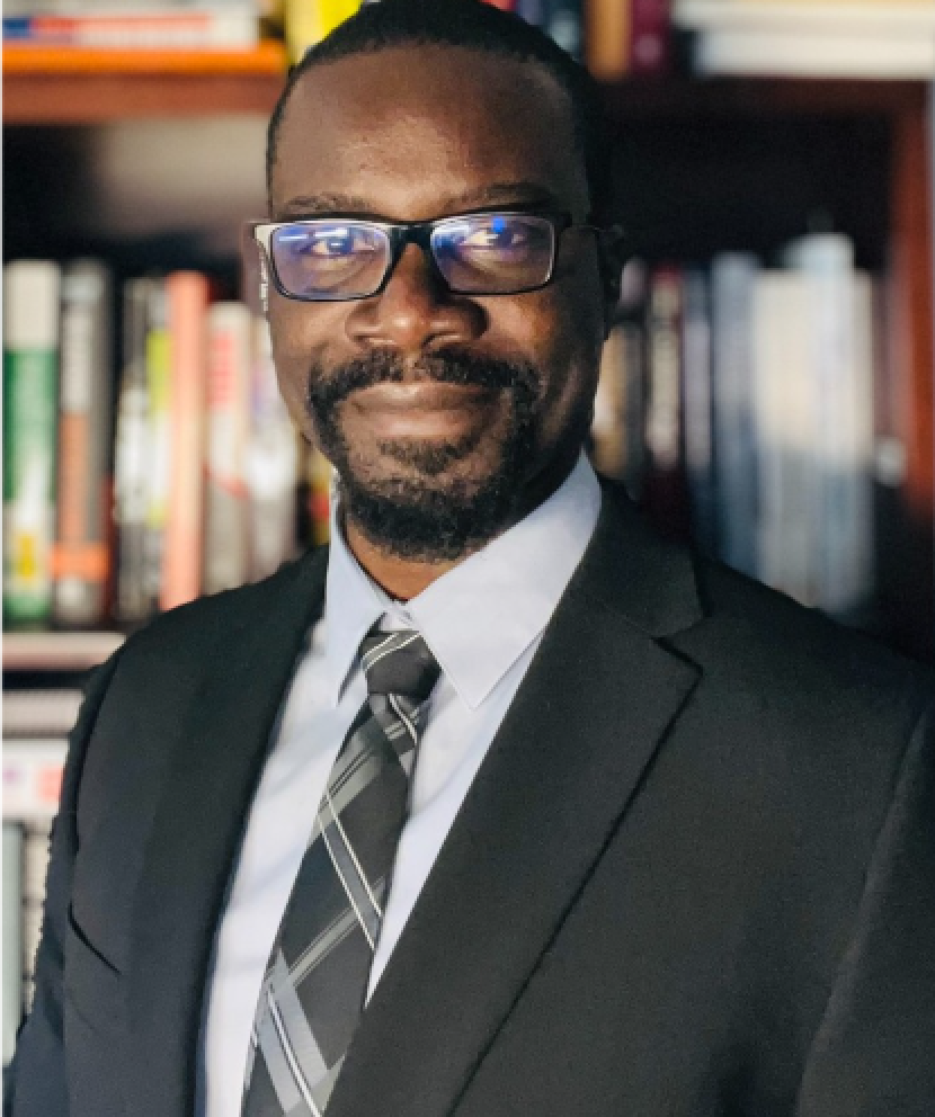 Head and shoulders shot of Emeka Obikwelu standing before a bookshelf.
