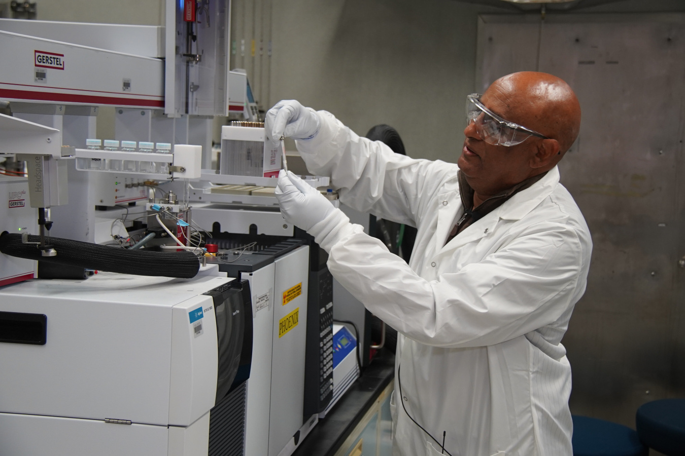 A scientist in a white lab coat and safety goggles performing the Stir Bar Method in a laboratory 