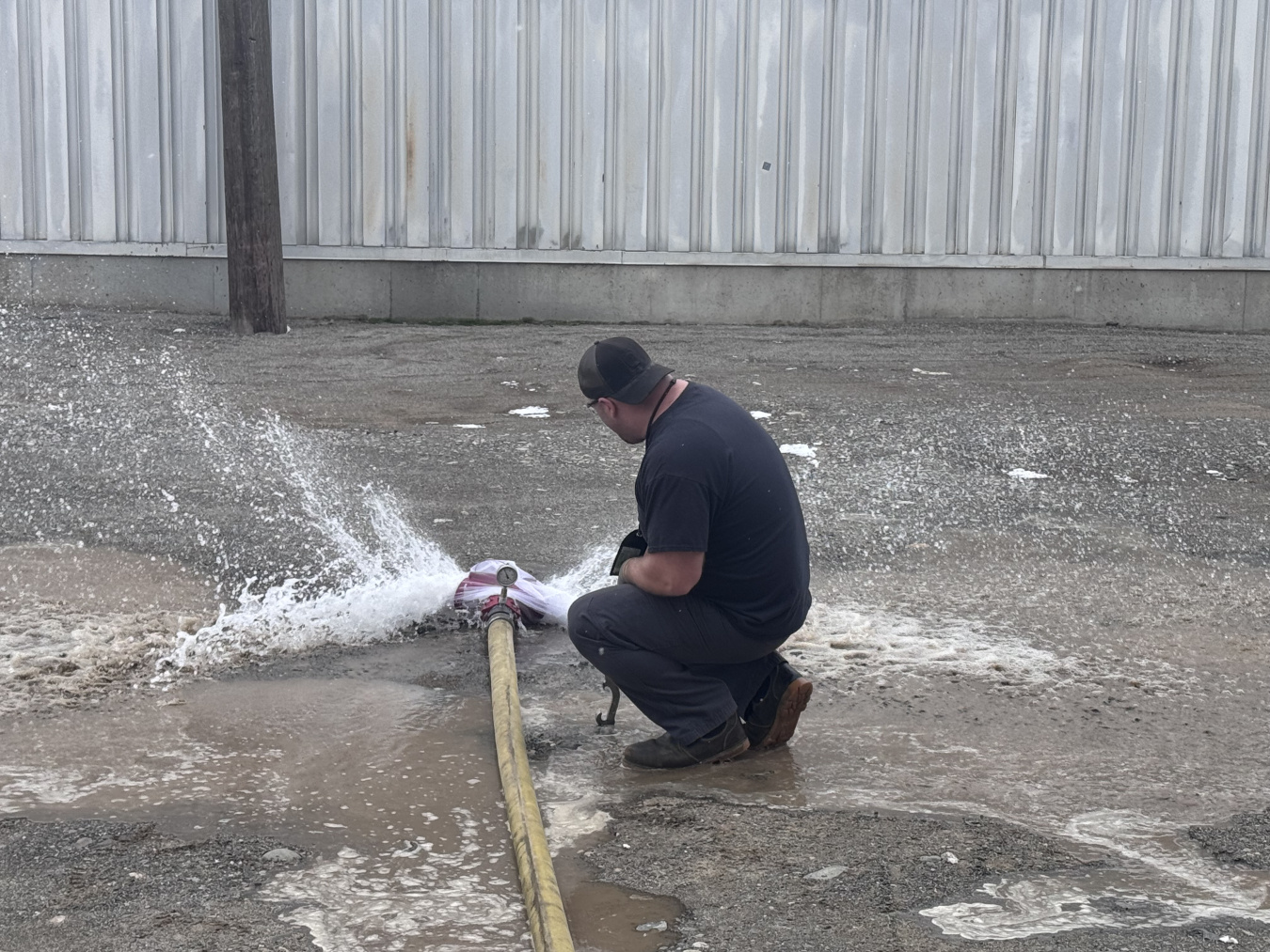 A worker sitting beside a large hose spraying water