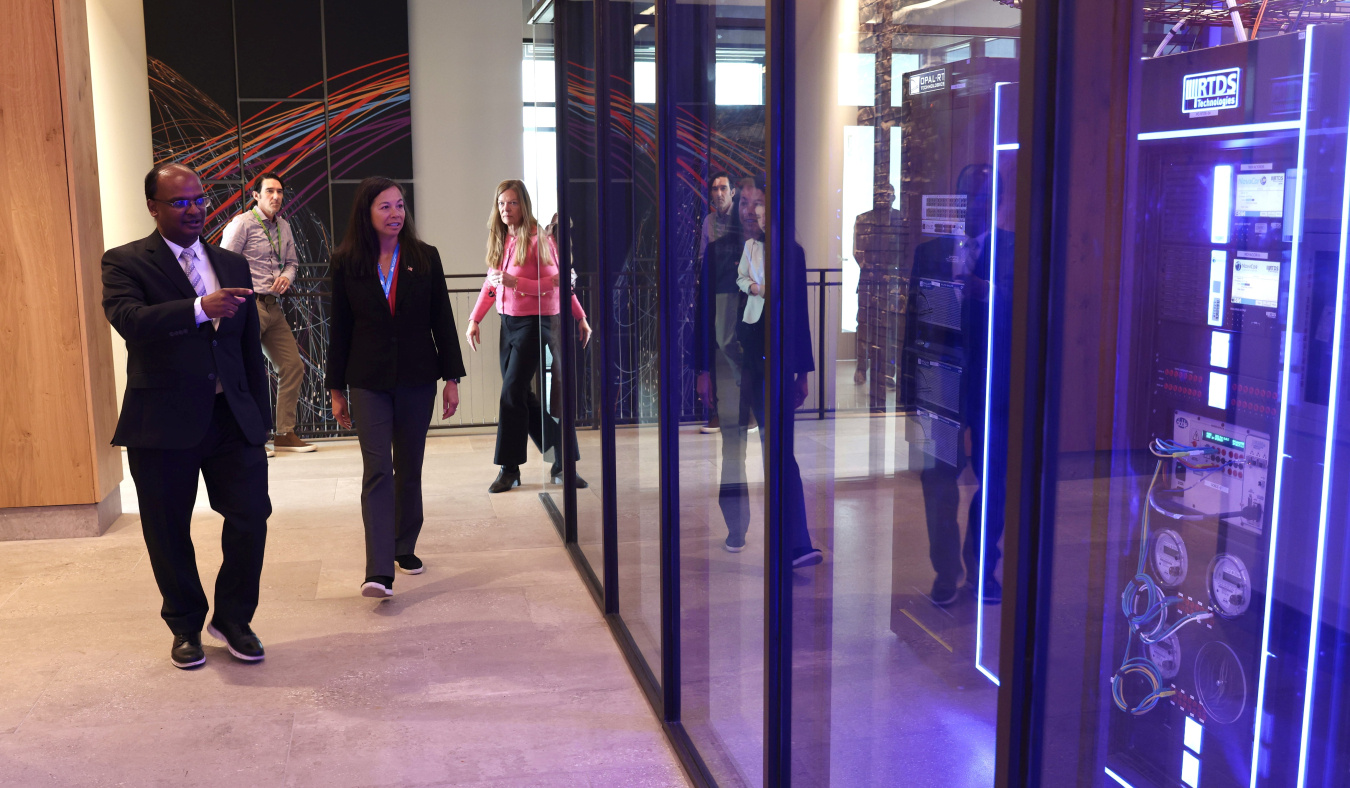 Two people in the foreground walk down a hallway at the Flatirons Campus at the National Lab of the Rockies to see the ARIES computer platform at the right.