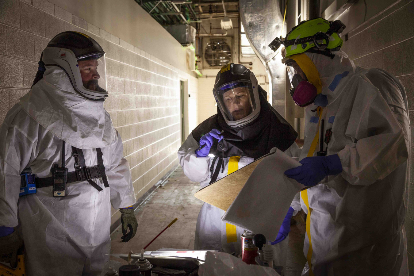 Employees in hazmat suits talking to eachother and looking at papers inside a facility building