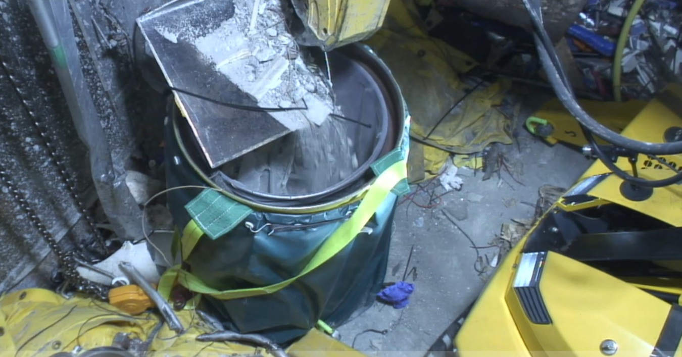 An attachment on a yellow robotic arm that scoops up debris 