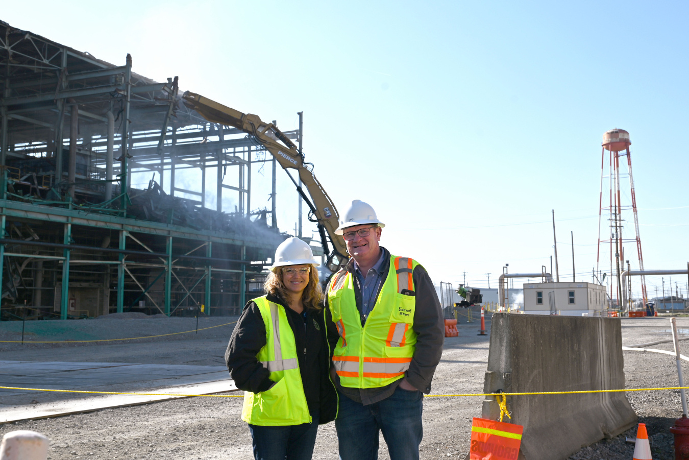 Two people in protective gear and white hard hats pose for a picture at the Portsmouth Site