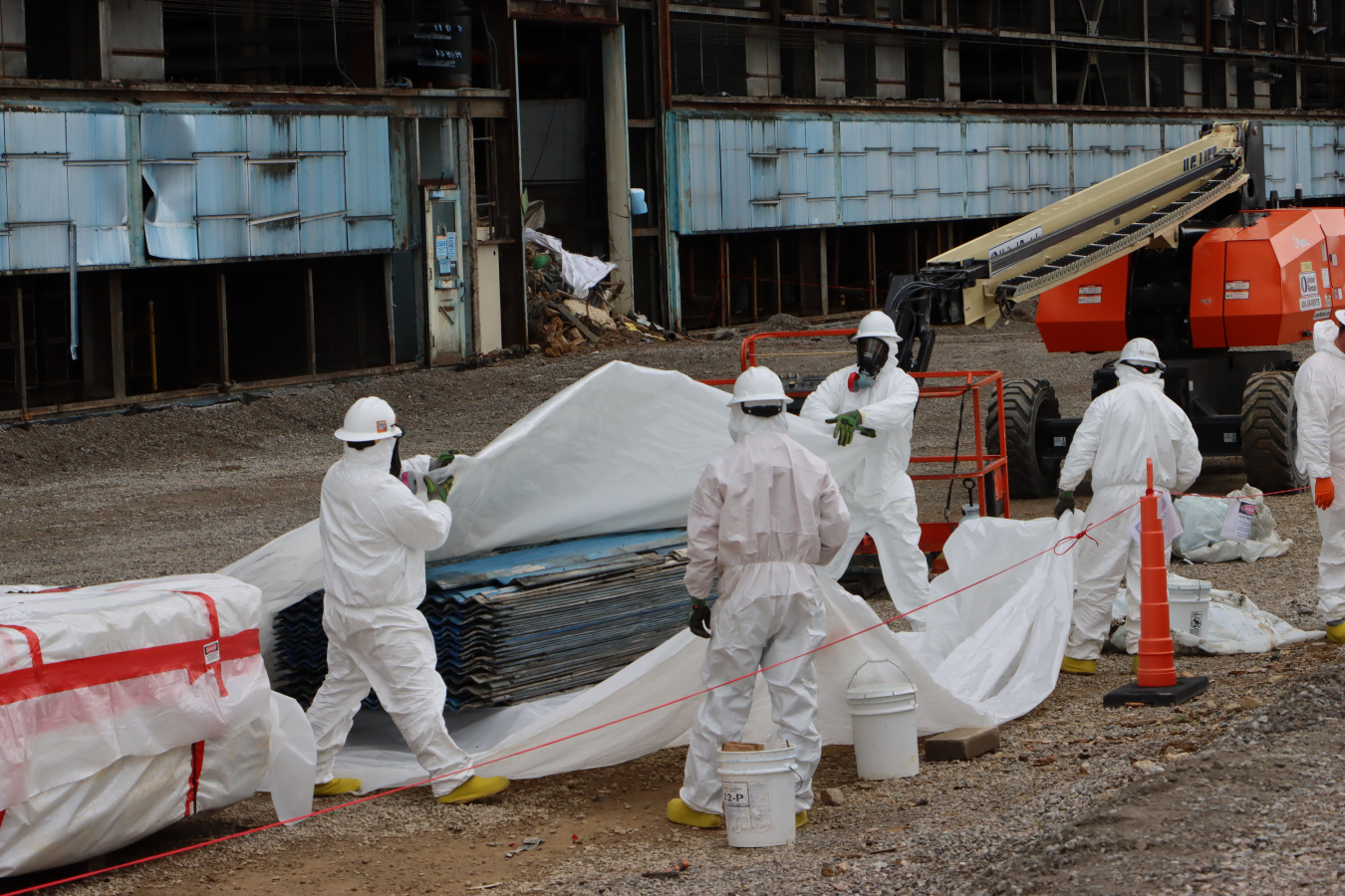 Employees in hazmat suits wrapping materials with a white cover