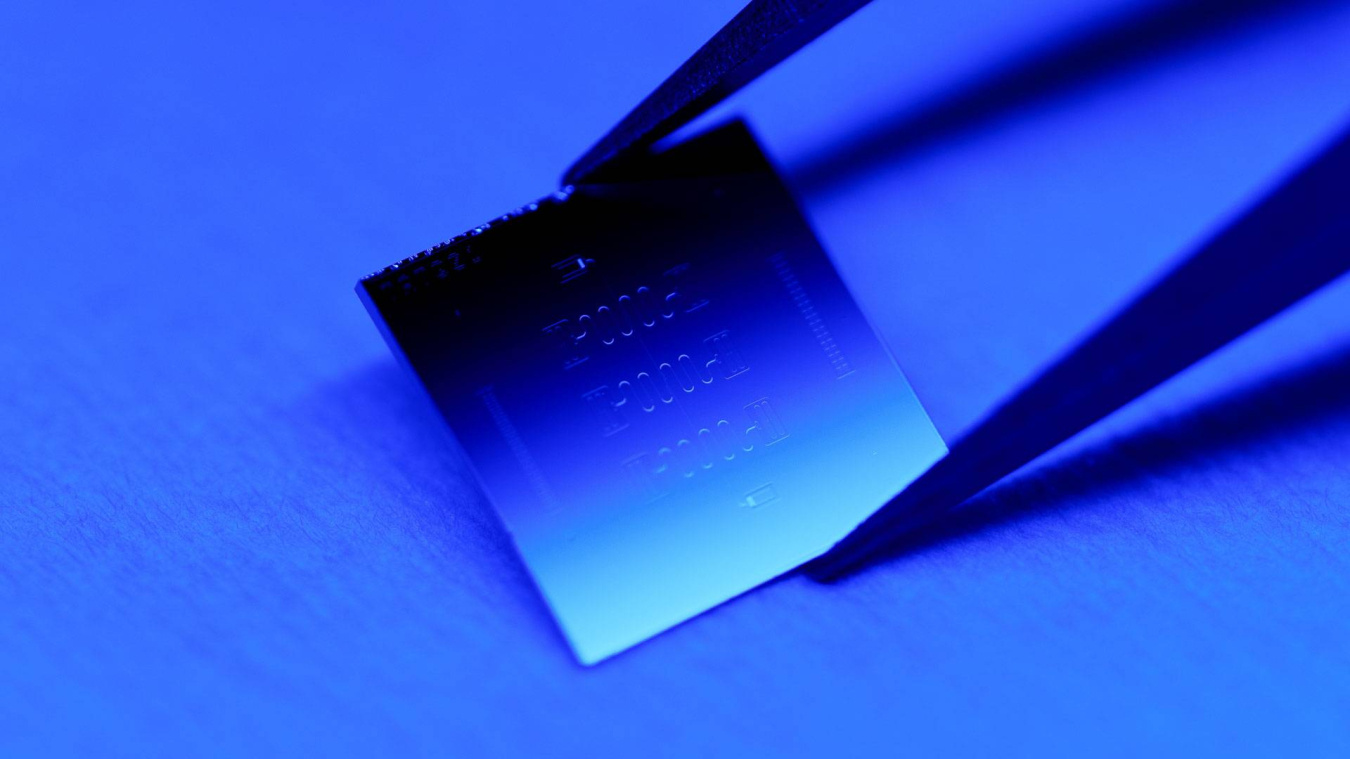  A computer chip being held by a pair of tweezers with a blue lighted background