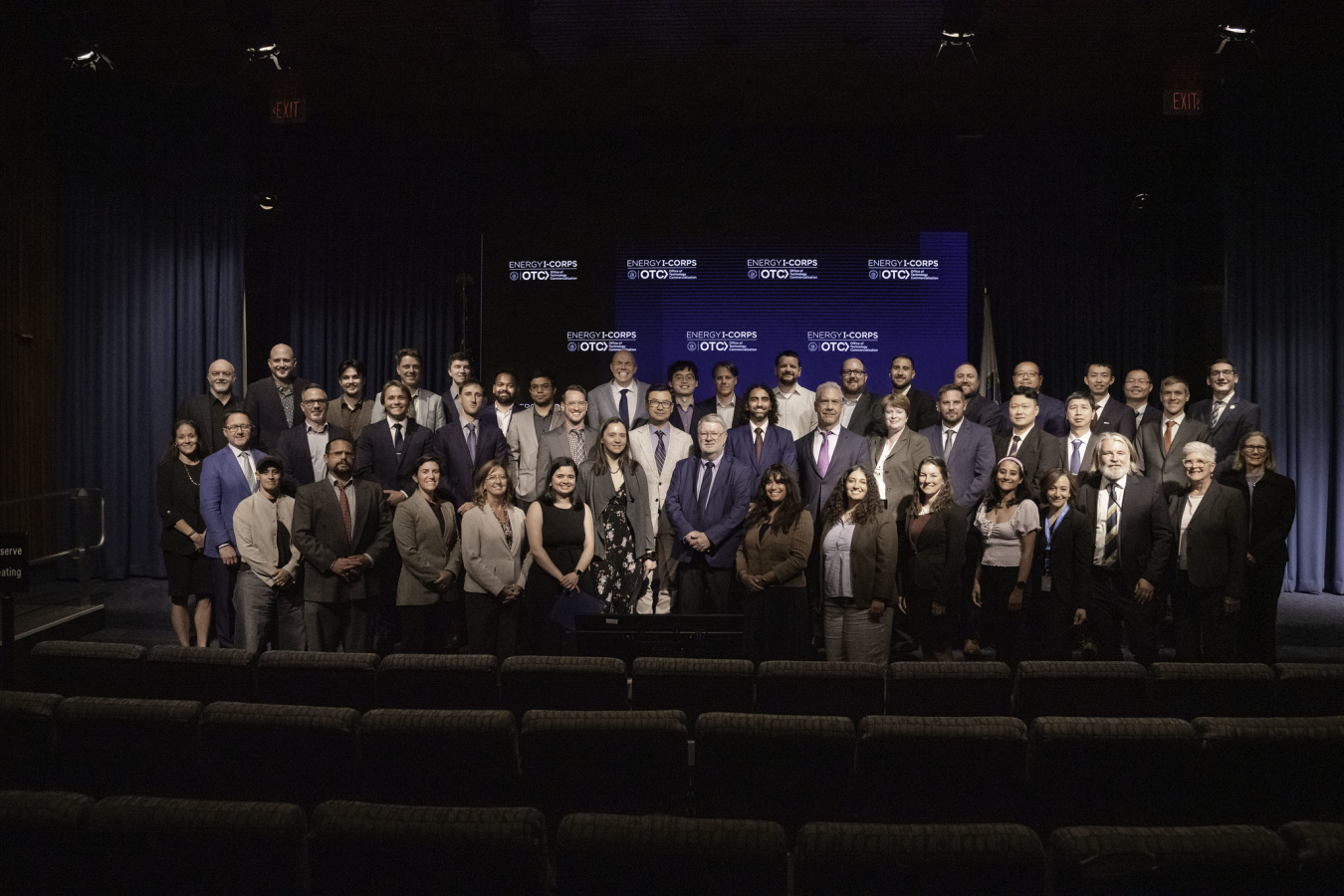 A group of approximately 45 people pose together on a podium with the Energy I-Corps logo displayed in the background. 