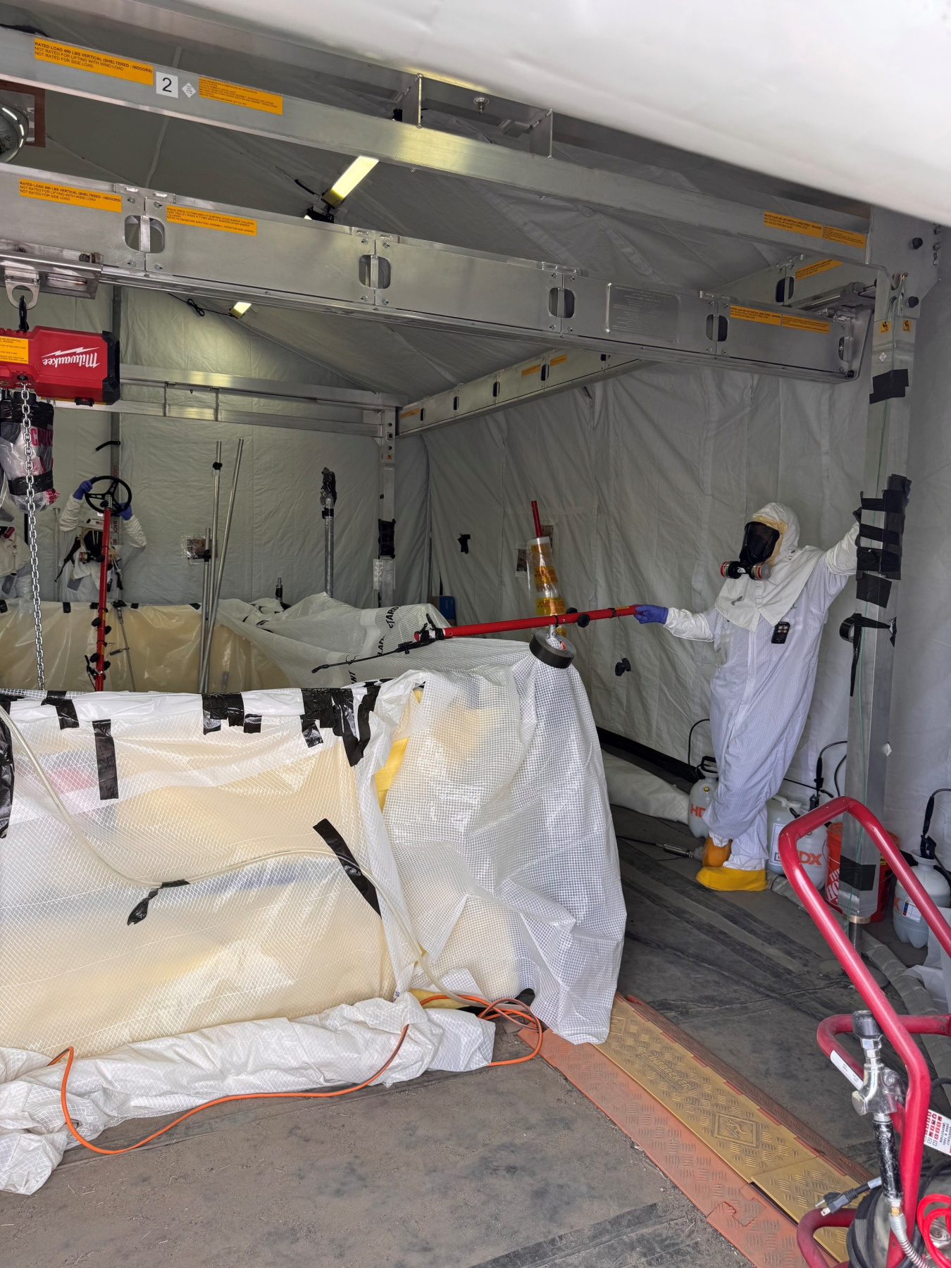 Employee in a hazmat suit using a long reach tool to clean a valve pit at the Hanford Site