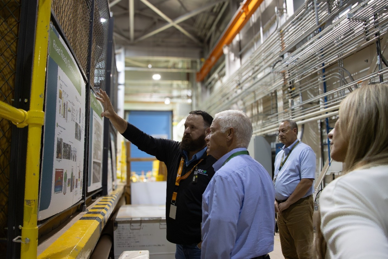 EM Assistant Secretary taking a tour of a fuel storage facility building with lots of pipes and signs on the wall