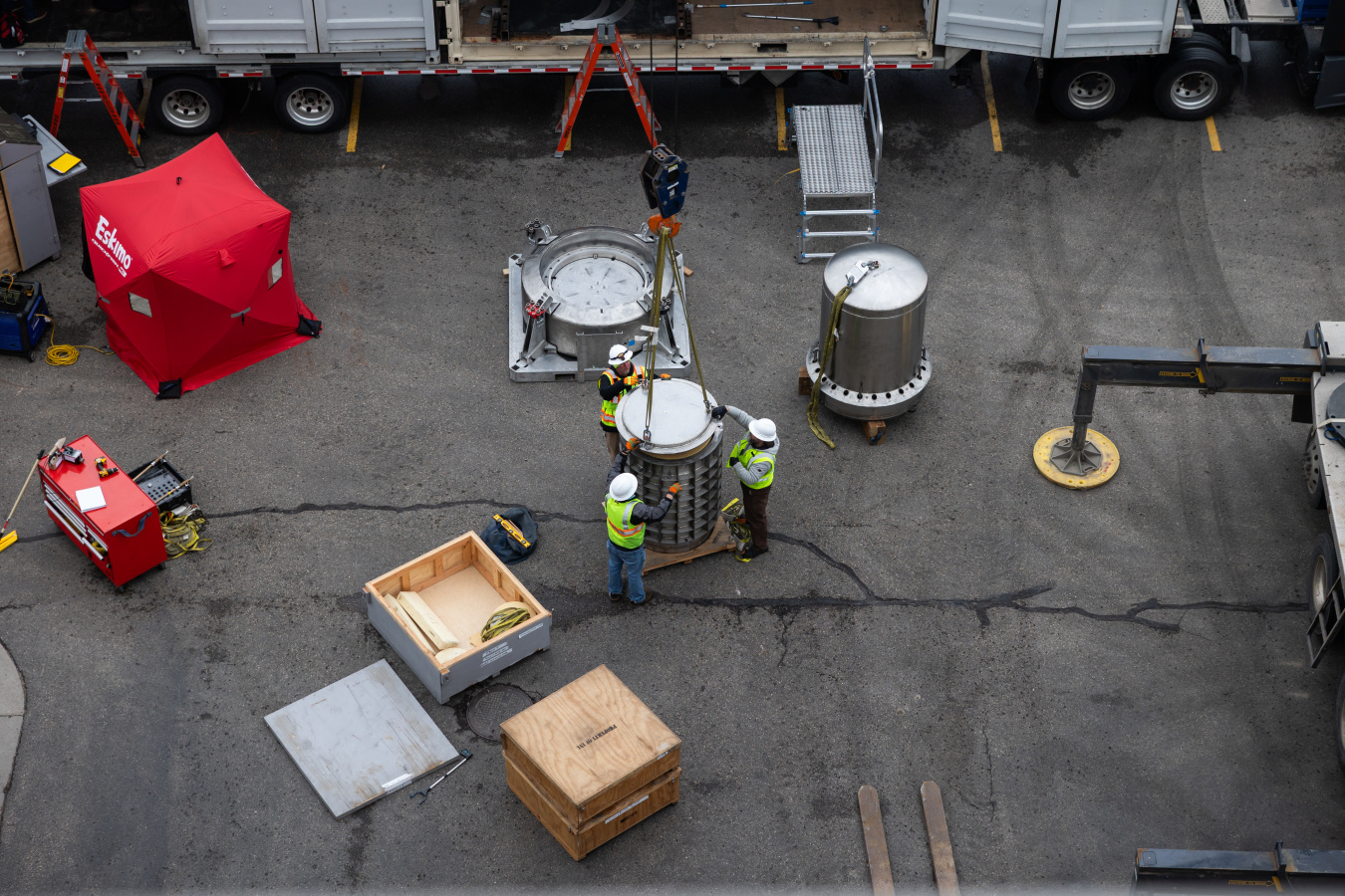 In a photo taken from far above, three men dressed in high-visibility clothing guide a transportation cask following the removal of the irradiator.