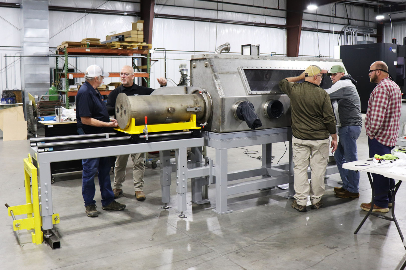 A large metal glovebox with five employees working on and around it