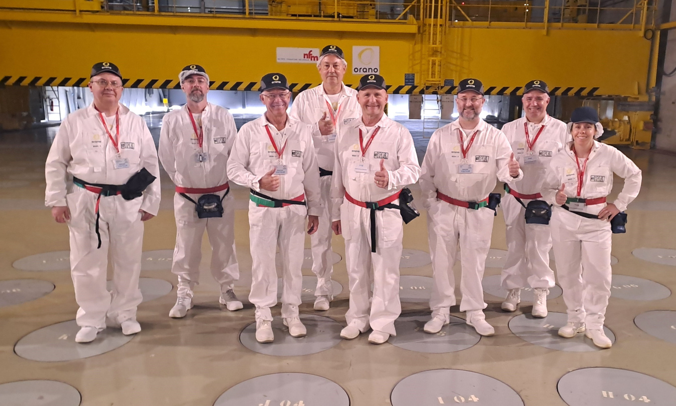 A group of professionals in white hazmat suits tour a lab building 