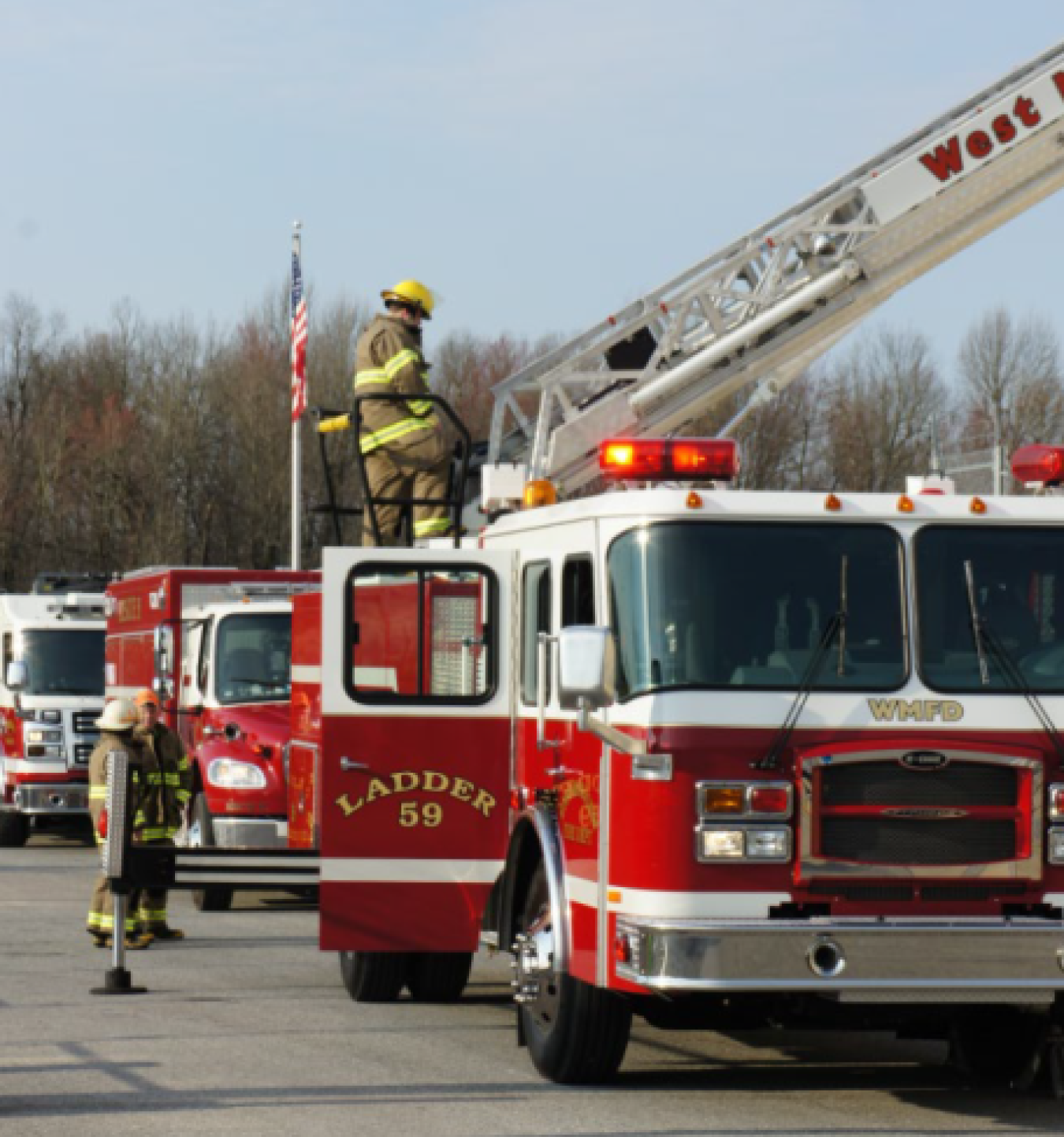 A firefighter on top of a firetruck with the ladder extended, he stands at the bottom of the ladder. 