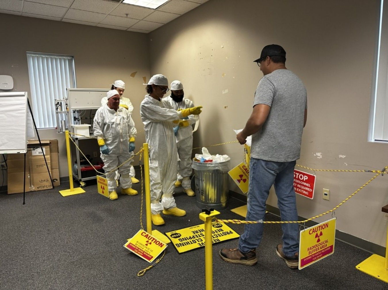 A group of employees in hazmat suits conducting a radiological training in a room with yellow caution signs