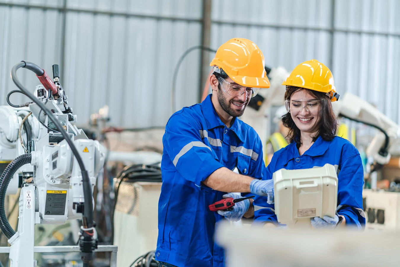 Two people wearing helmets and safety gear in manufacturing setting