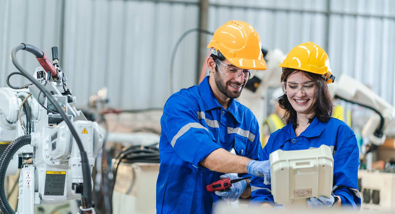 Two people wearing helmets and safety gear in manufacturing setting