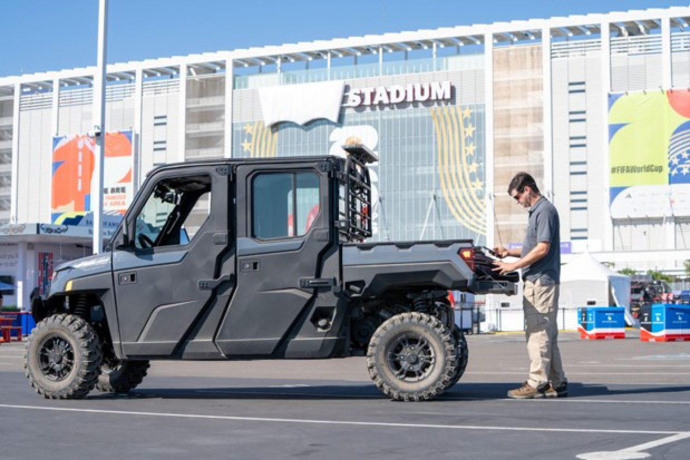 A man looks at a tablet next to a small utility vehicle. They are in front of Levi's Stadium in Santa Clara, California.