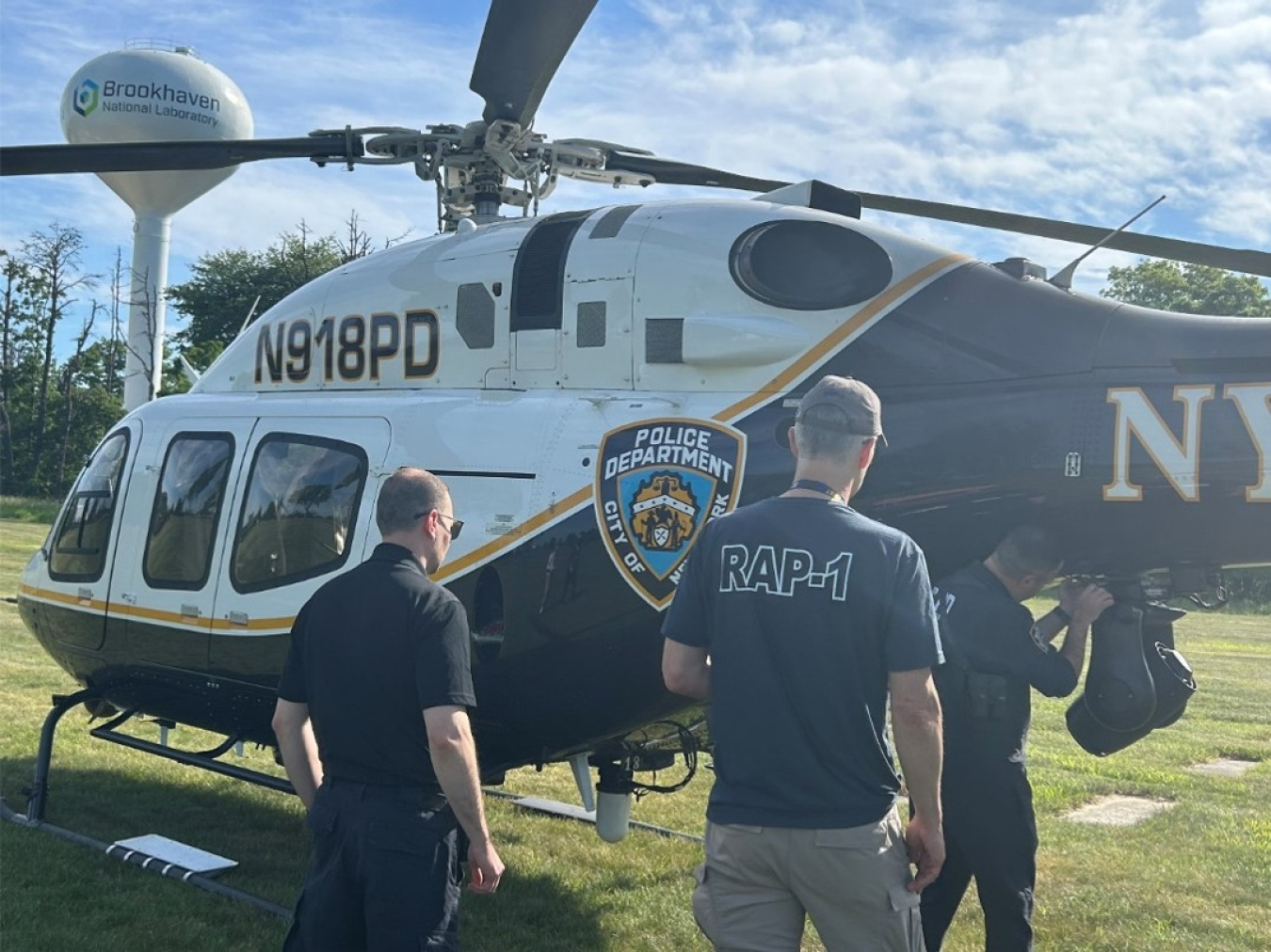 Men prepare a New York Police Department helicopter for flight. One has RAP-1 written across the back.