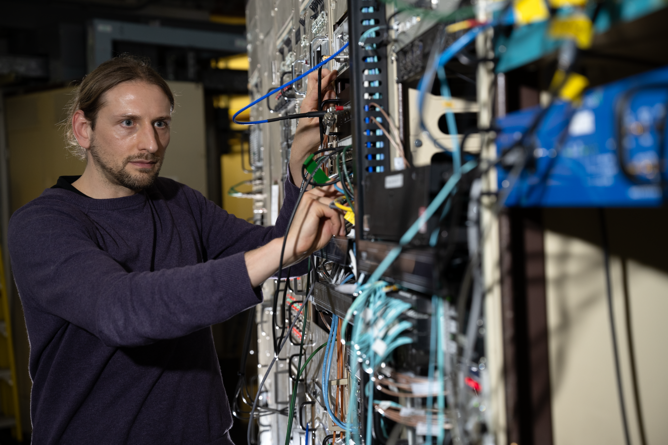 Researcher connects and adjusts cables on computer and networking equipment in a laboratory.