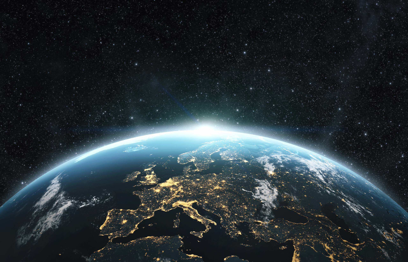 View of Earth from space at night, with illuminated cities across Europe beneath a star-filled sky.