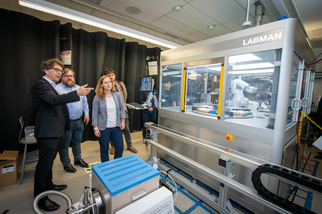 Researchers observe an automated robotic laboratory system performing experiments. 