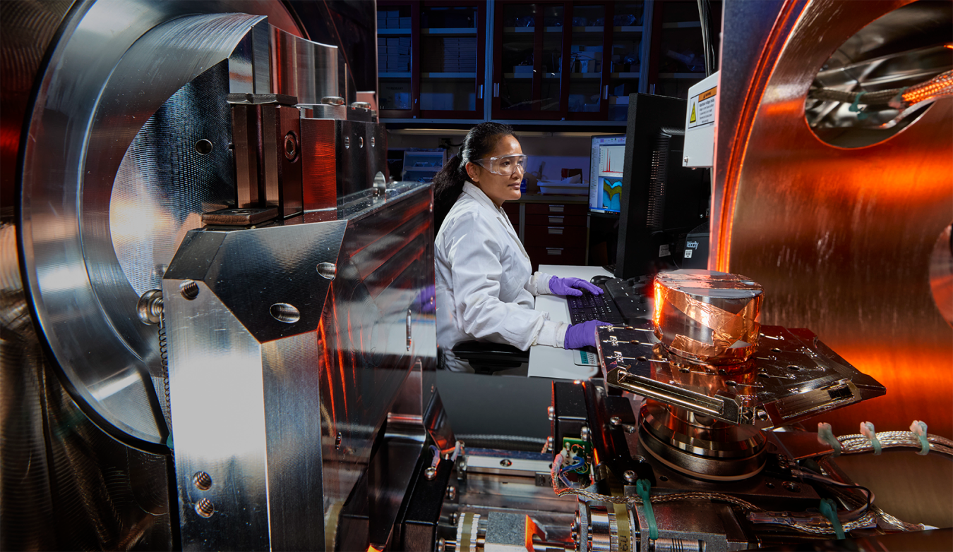 Scientist operates advanced laboratory equipment while monitoring data on a computer. 