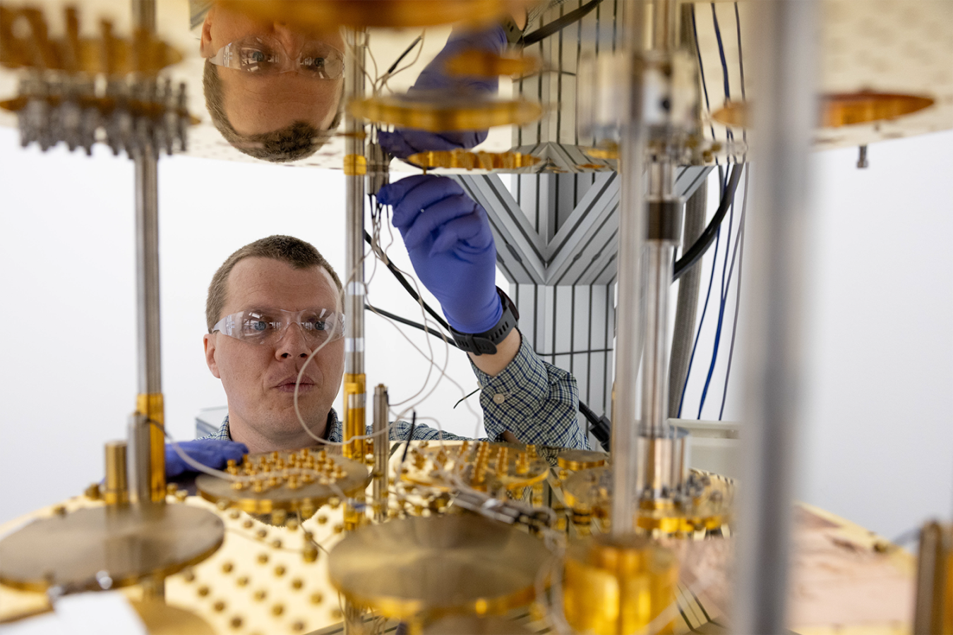 Researcher wearing safety glasses and gloves works with components of a quantum computing system. 