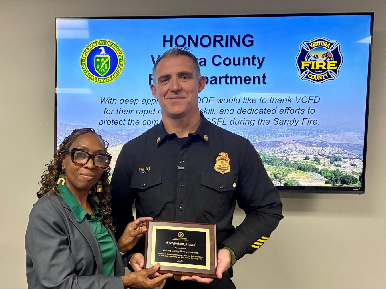Two professionals posing for a photo, the man on the right is holding an award plaque