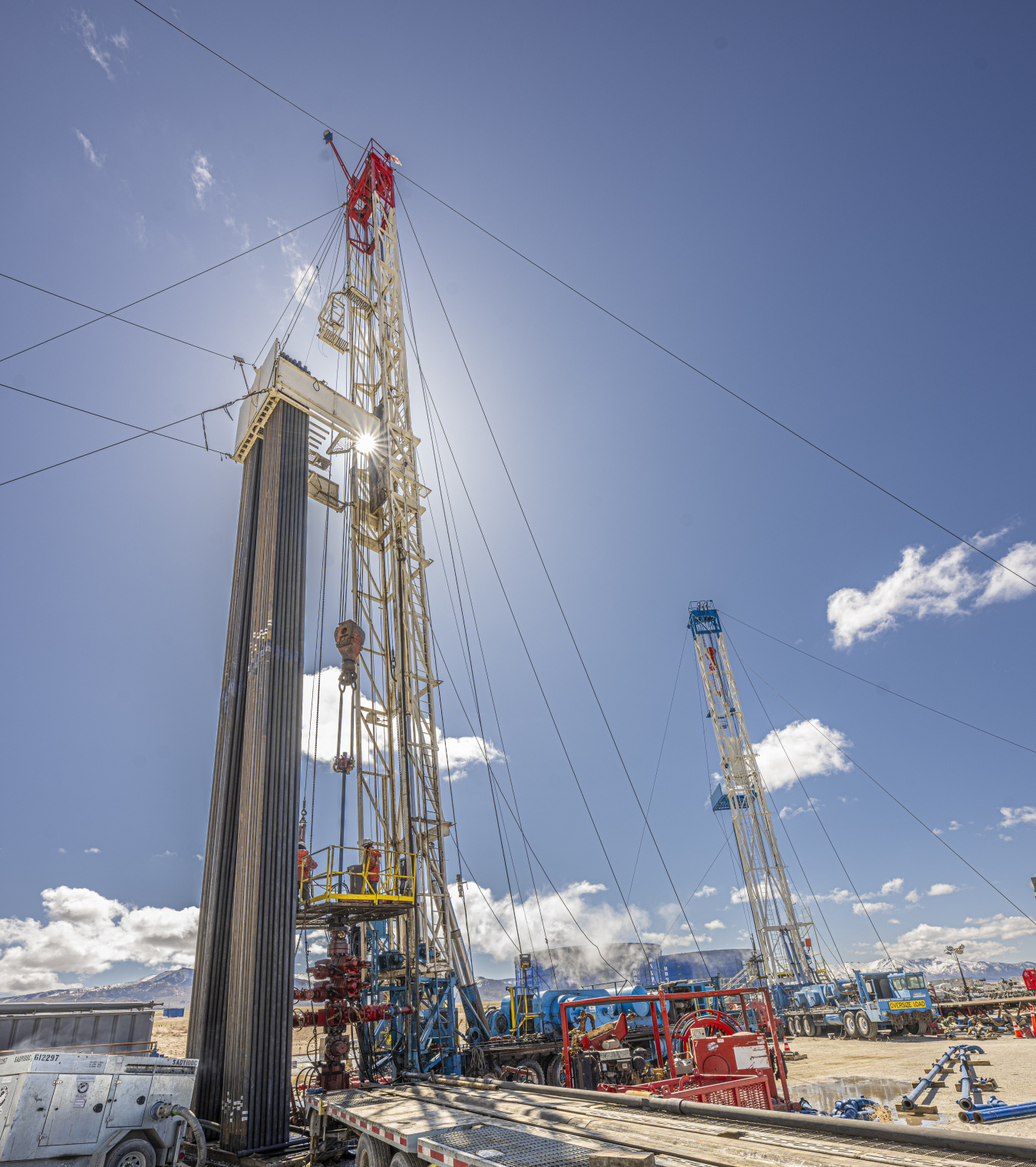 Close-up photo of a drill rig at the FORGe site, with a blue sky above and the sun shining directly behind the derrick (mast).