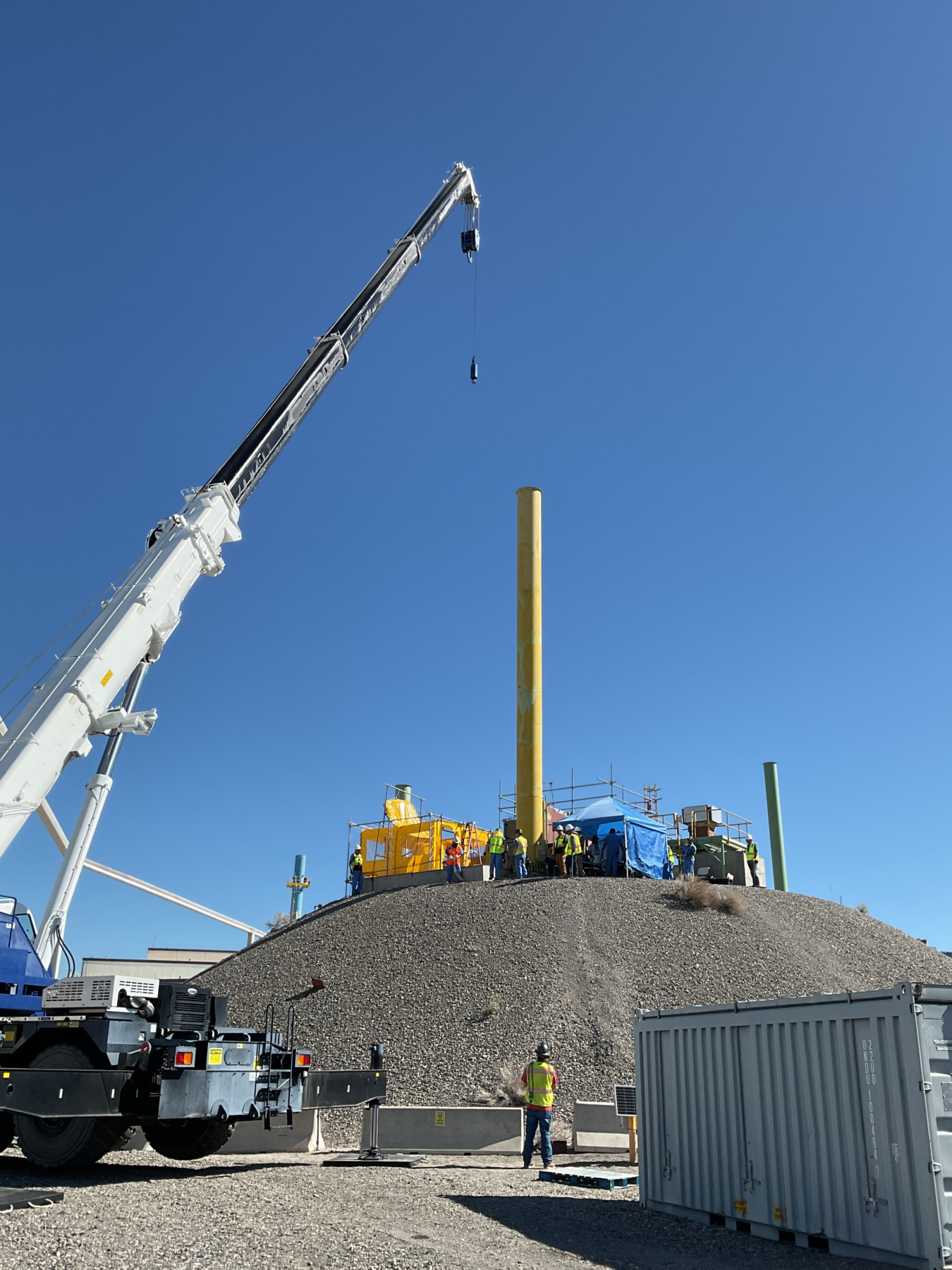 A large white crane opening a calcine bin on top of a large mound outside at the Idaho Site