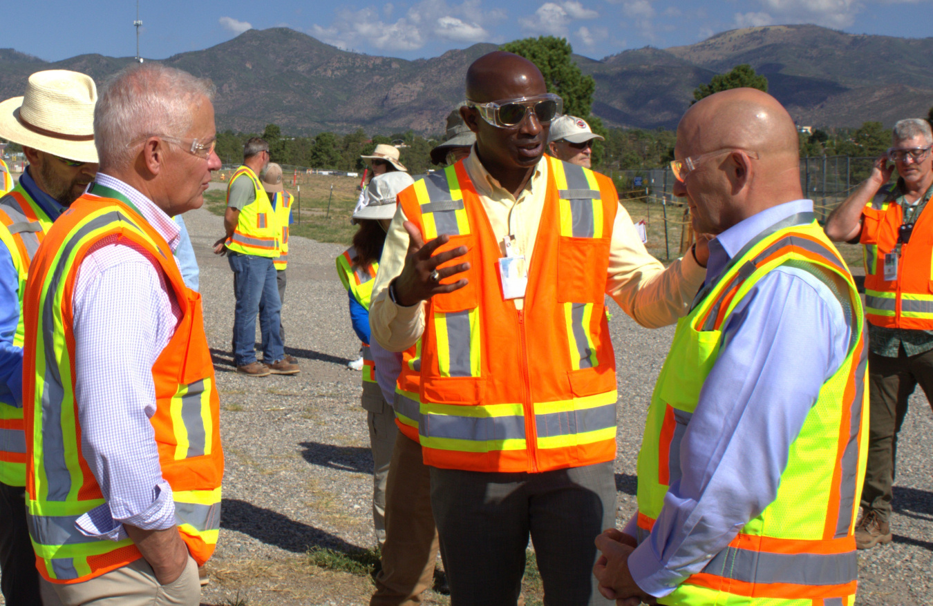 A group of professionals in safety vests stand outside talking at the Los Alamos Site