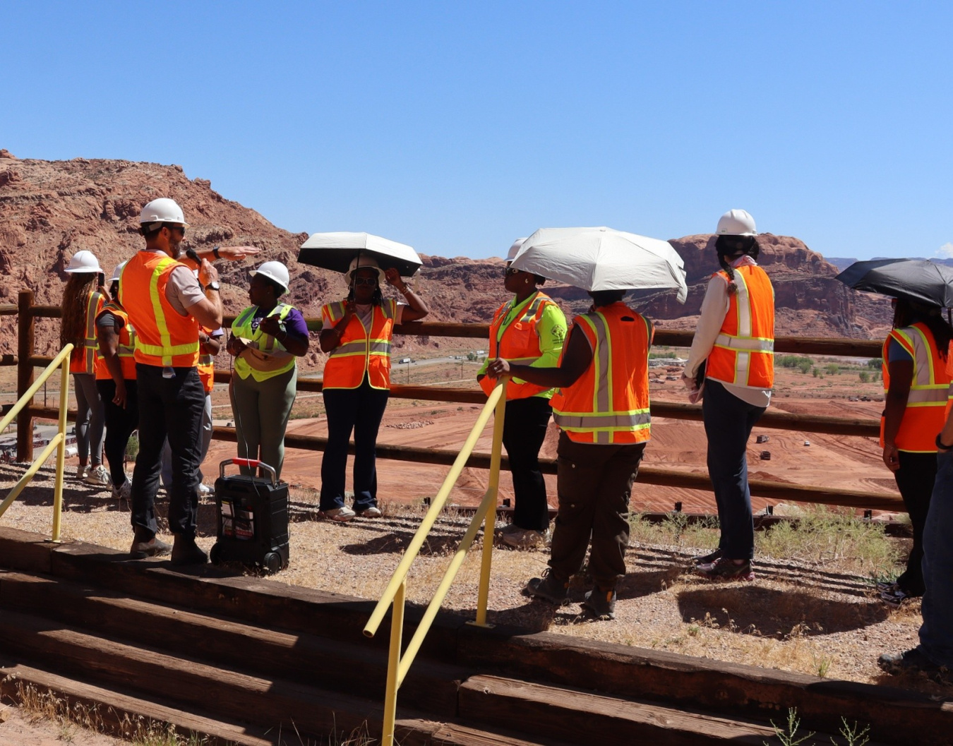 A group of interns in orange safety vests and hard hats tour the Moab Site