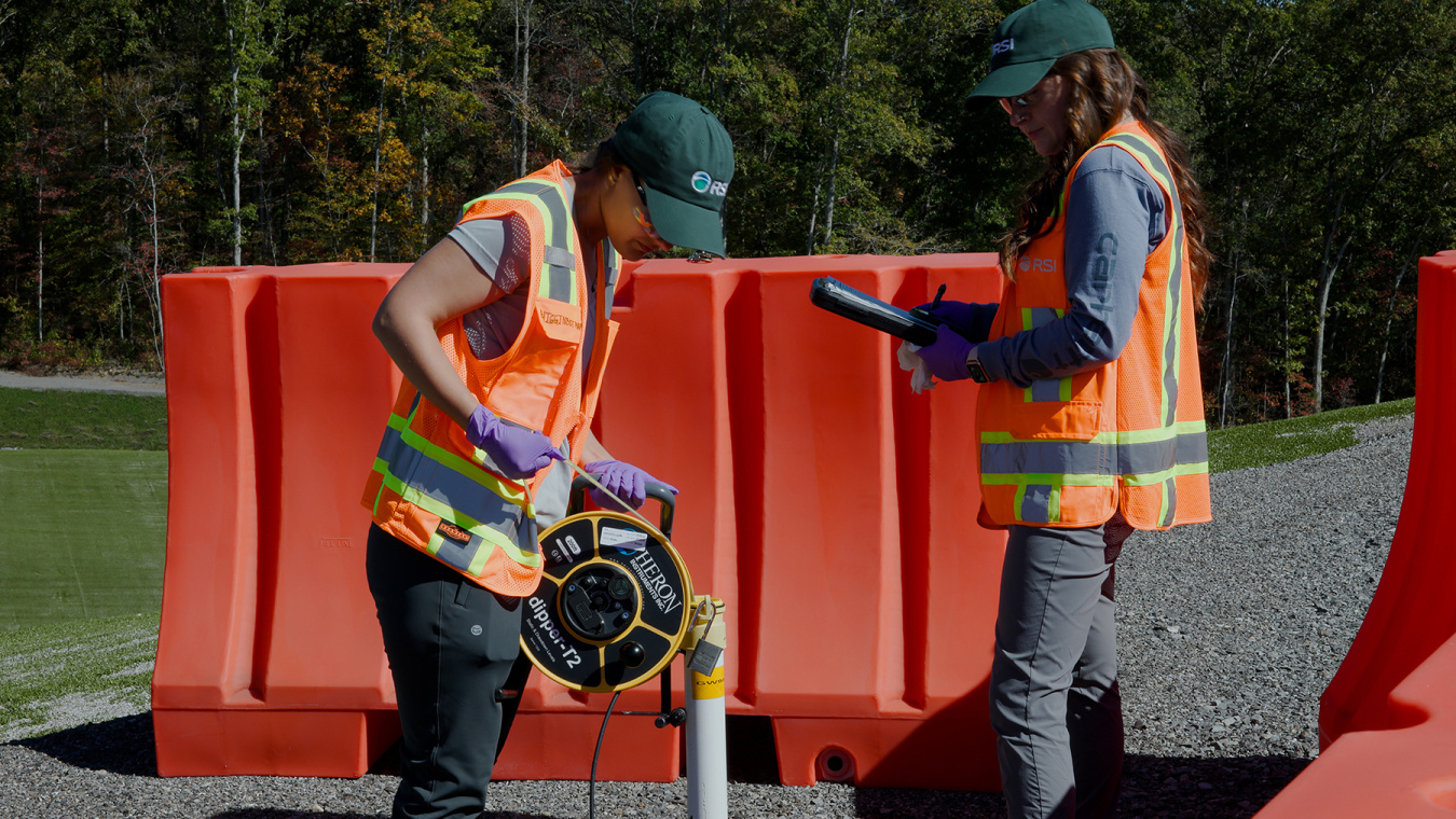 two employees in orange safety vests conduct groundwater sampling at the Oak Ridge site