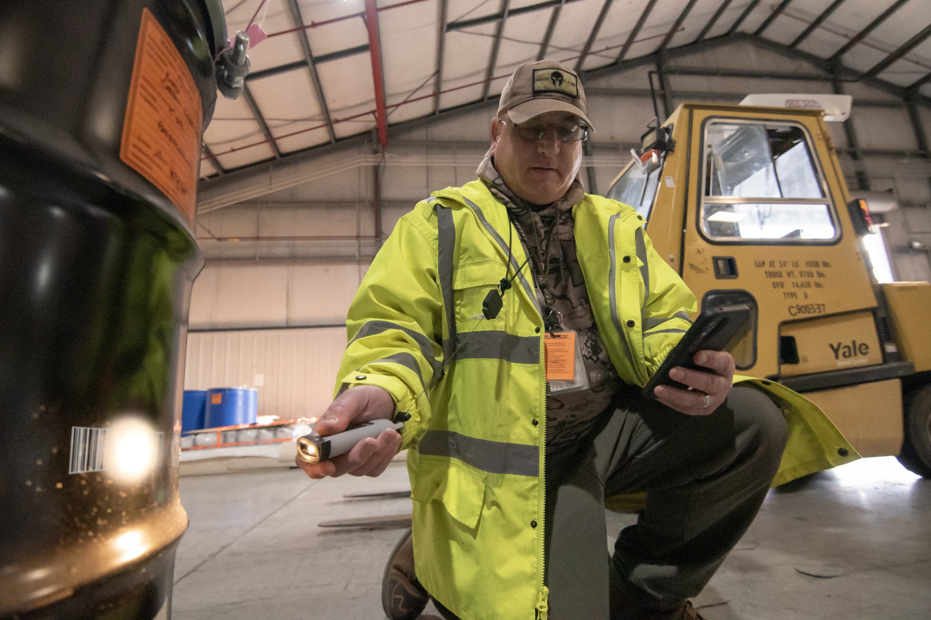 A man in a yellow jacket using a barcode scanner on the side of a black container