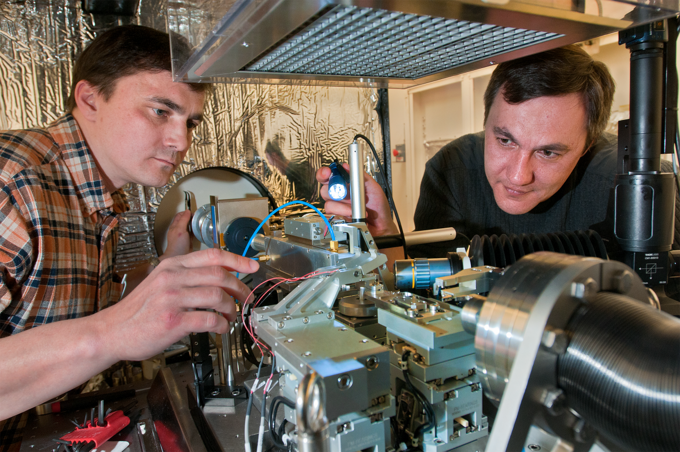 Two researchers examine and adjust precision equipment in a laboratory. 