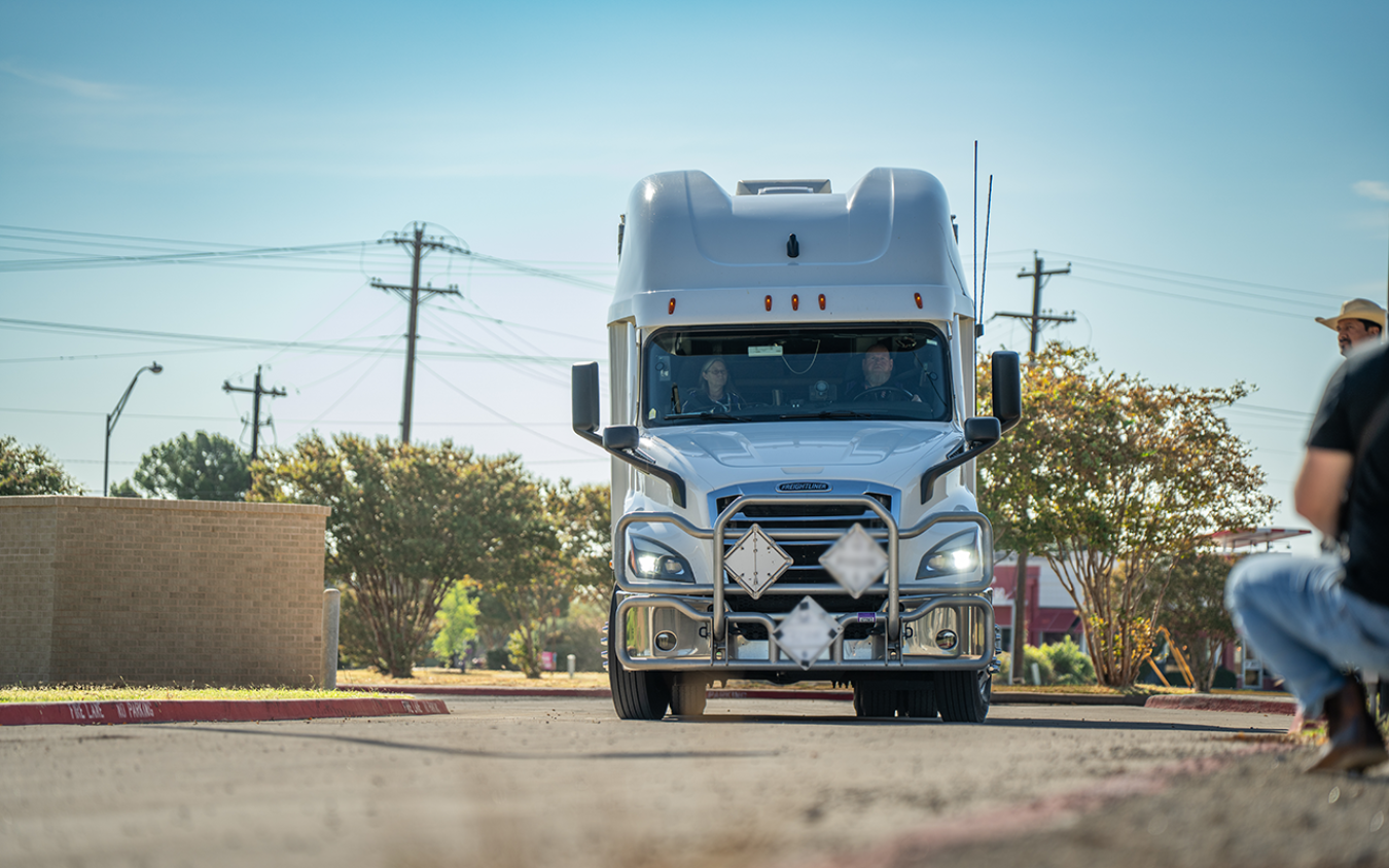 A semi truck approaches while people stand off to one side.